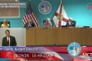 John Quinn appears in a tiny window on the lower-left of the screen with Monroe County Commissioners appearing on the dais behind him.