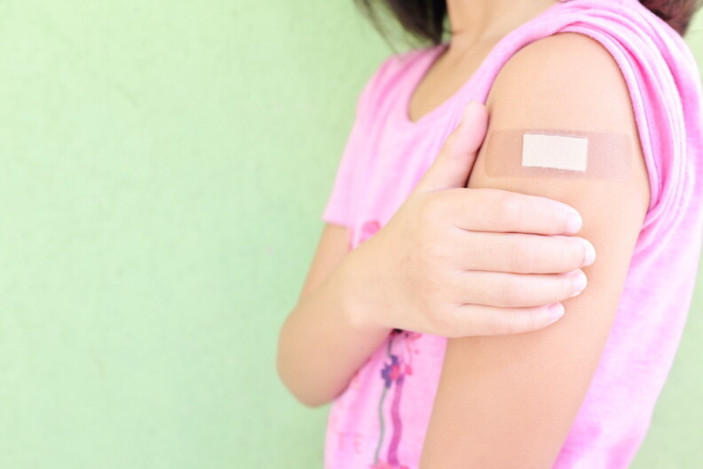 Closeup of shoulder of a vaccinated young Asian girl with adhesive bandage in thumbs up.