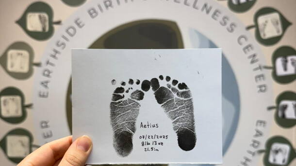 A hand is shown holding up a piece of paper showing baby ink footprints.