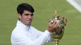 Carlos Alcaraz of Spain smiles as he holds up his trophy for the photographers after defeating Novak Djokovic of Serbia in the men's singles final at the Wimbledon tennis championships in London, Sunday, July 14, 2024. (AP Photo/Mosa'ab Elshamy)