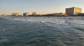 Beaches with people swiming and along the coastline, skyline in the background of buildings