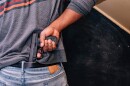 A man is seen from the back tucking a handgun into his jeans