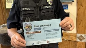 A person in a police uniform holds a large blue envelope.