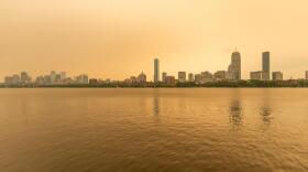 The Boston skyline along the Charles River as seen around noon on Wednesday as wildfire smoke from Canada creates a yellow haze. (Jesse Costa/WBUR)