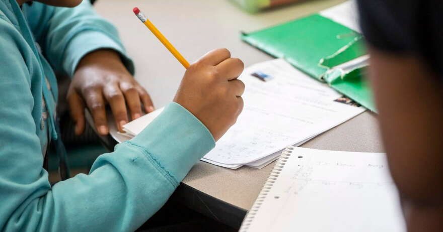 A student writes with a pencil at a table.