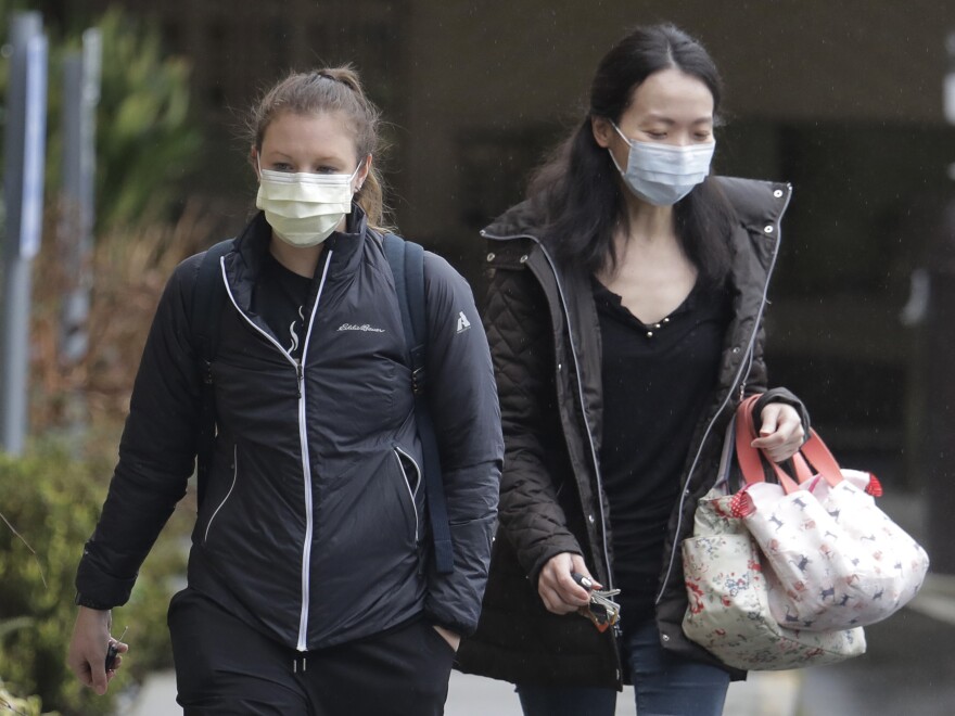 Two women wearing masks walk away from the Life Care Center in Kirkland, Wash., near Seattle. An outbreak of the coronavirus is cited as the cause for the deaths of at least two residents at the center.