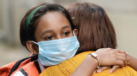 Two children hugging and wearing masks. 