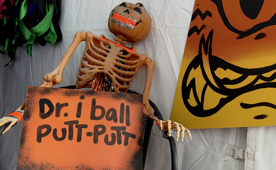 A skeleton holding a sign next to a poster of a candycorn