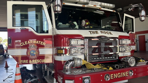 red-and-white Clearwater Fire & Rescue fire truck parked inside a fire station with its front doors open. Firefighting gear lays on the ground around.