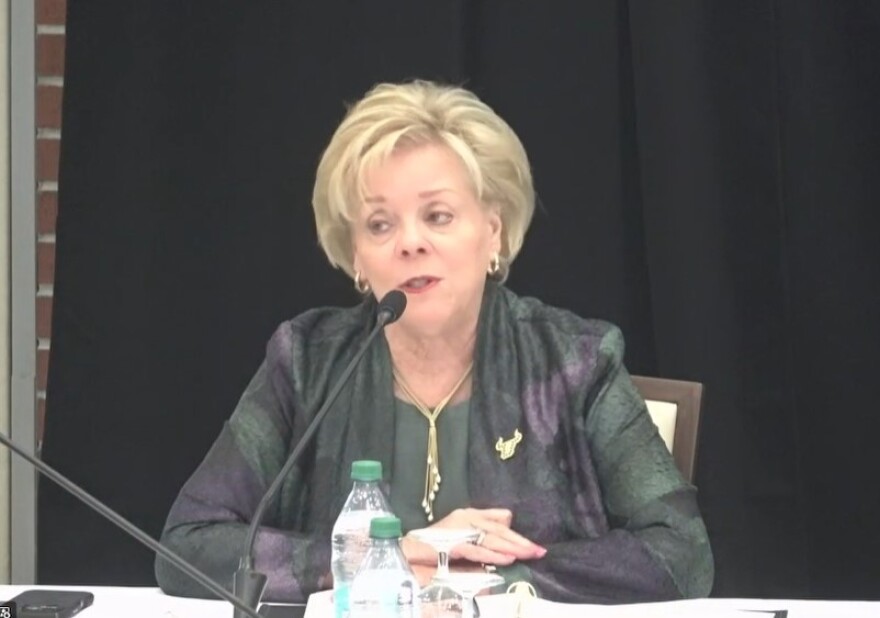 A blonde woman dressed in dark green speaks at a mic