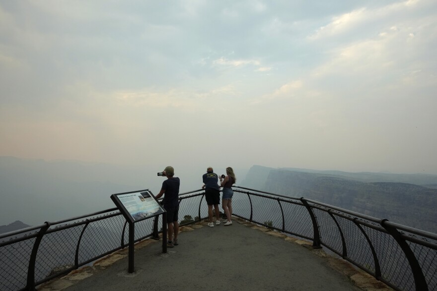 Smoke from the Dragon Bravo Fire moves over the Grand Canyon from the North Rim blocking the view for tourists at the Desert View overlook Monday, July 14, 2025, in Grand Canyon National Park, Ariz. (AP Photo/Ross D. Franklin)
