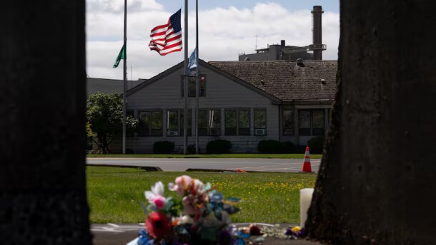 The Washington state flag, American flag and Nippon Dynawave flags fly at half-staff while flowers mark a makeshift memorial on old mill equipment in front of Nippon Dynawave Packaging Co. for the victims of the May 26 chemical disaster, in Longview, Wash., on May 29, 2026.