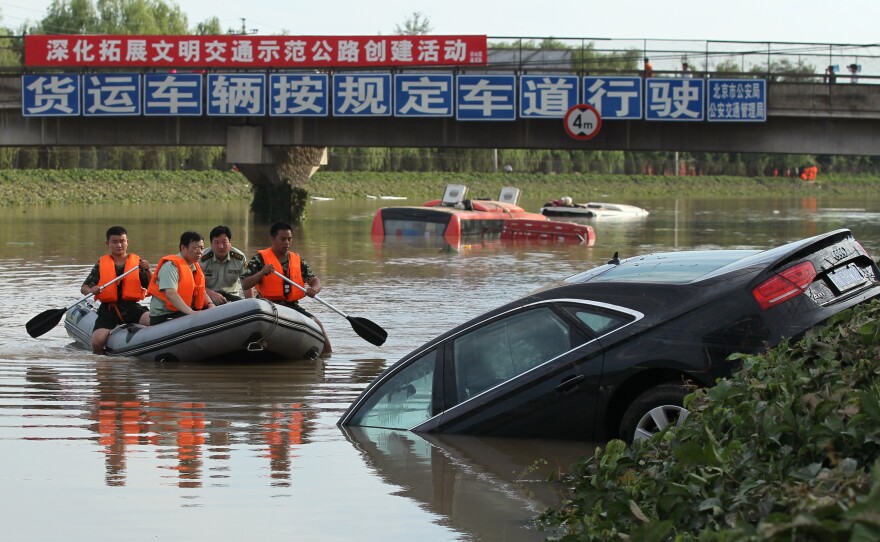 A rescue boat approaches a partially submerged car on a highway in the Fangshan District of Beijing.