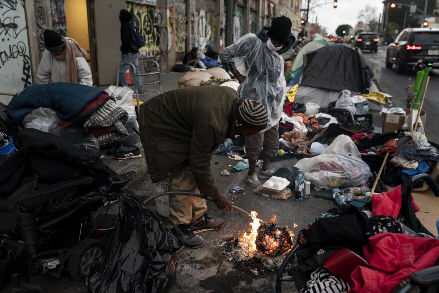 Robert Mason, a 56-year-old homeless man, warms up a piece of doughnut over a bonfire he set to keep himself warm on Skid Row in Los Angeles, Tuesday, Feb. 14, 2023.