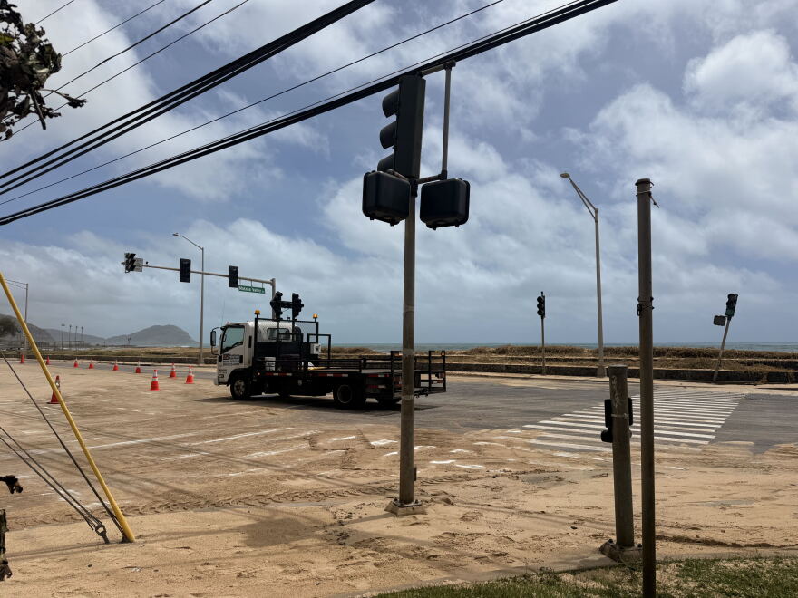 Crews work to remove sand from high surf at the intersection of Mākaha Valley Road and Farrington Highway.