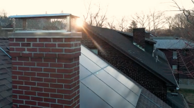 The sun peeks between two homes, shining on rooftop solar panels.