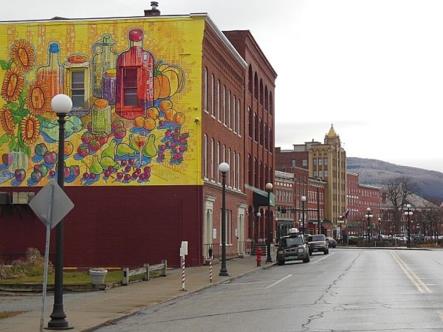 A photo of a downtown street lined with brick buildings, with a mountain visible over the top of them, and a mural of food and drink on the side of one building. 