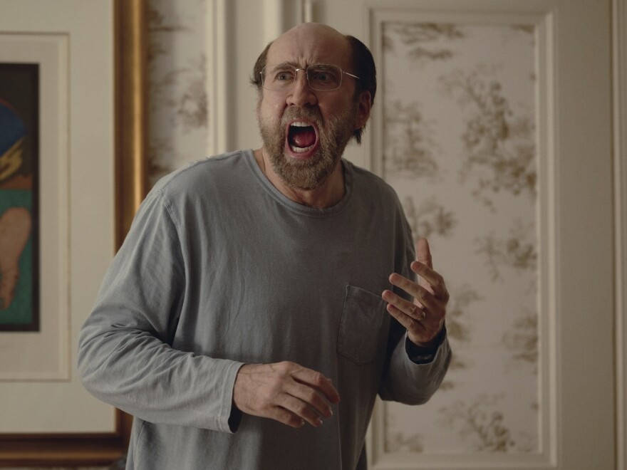 An balding older man with glasses screams in fright while standing in the living room of a suburban home.