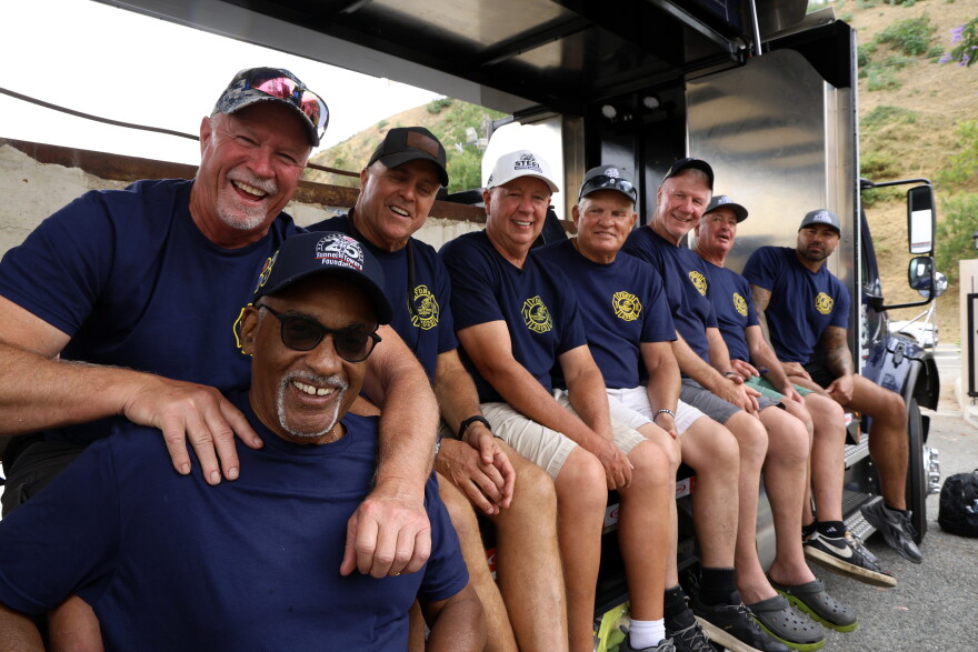 A row of men in blue T-shirts sit on a truck bed