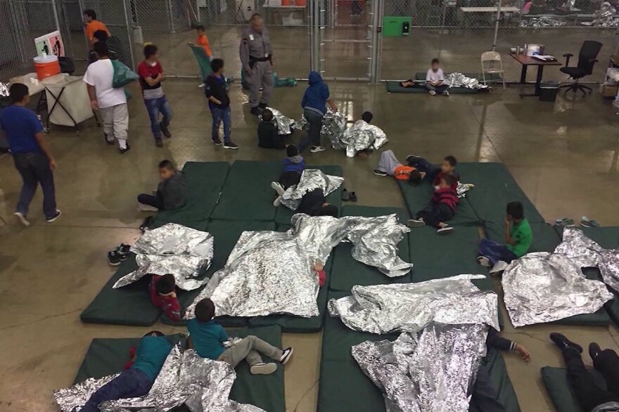 Group of migrant children together on mats with silver shock blankets. 