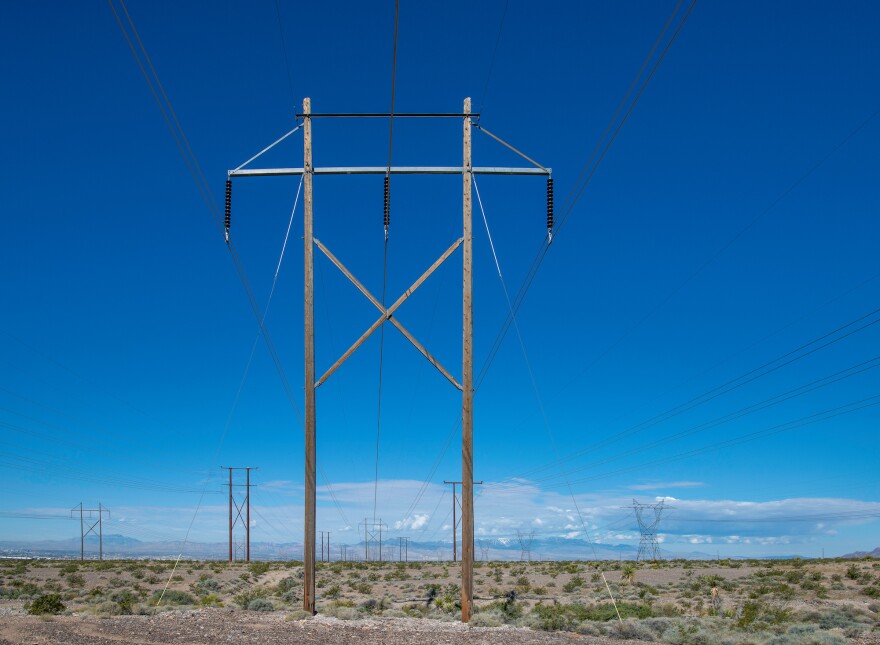 A field of high voltage power lines in a desert landscape during a blue-sky day.