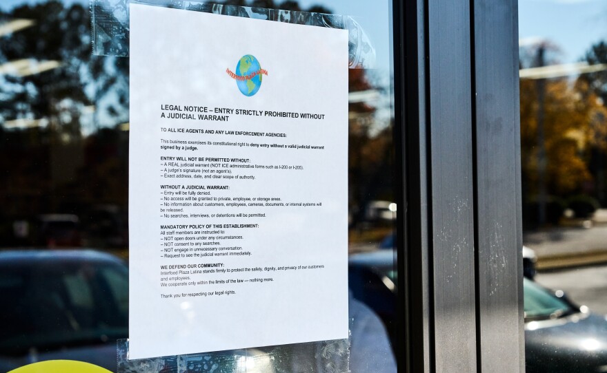 A hispanic grocery store employee puts up a sign on the door stating their refusal to allow ICE entry without a warrant.