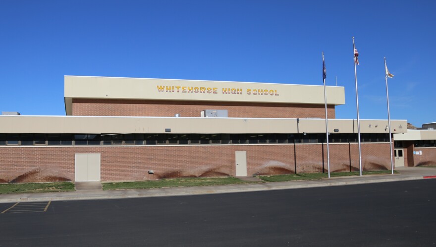 A large brick building with the words “whitehorse high school” on it and flags flying.