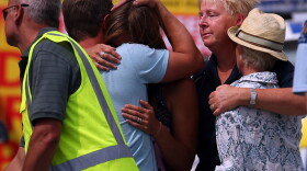 People grieve outside New Zealand's Muriwai Surf Lifesaving Club after the fatal shark attack at Muriwai Beach on Wednesday.