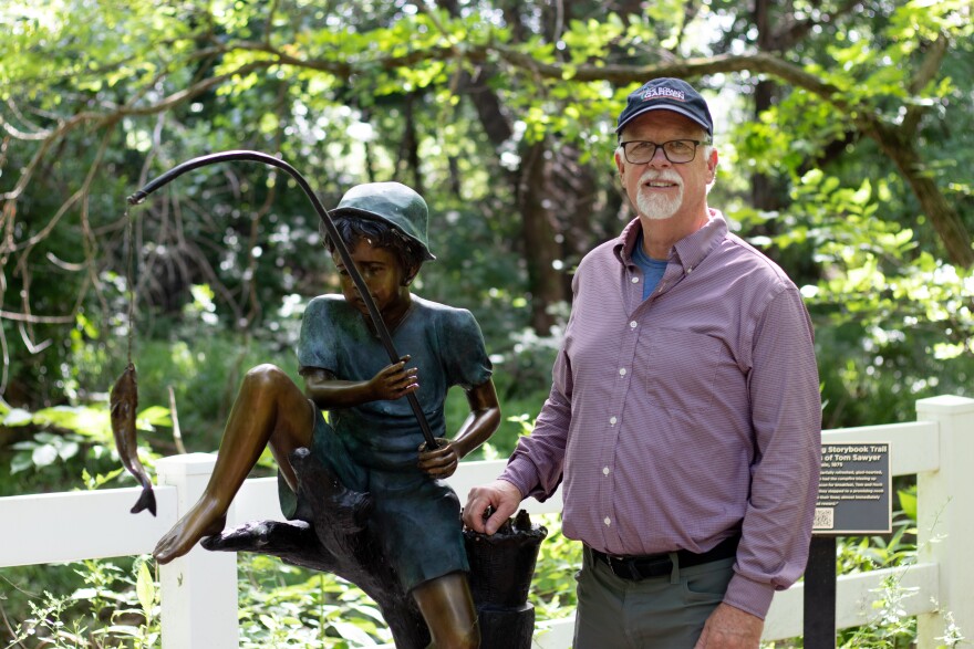 Director Lou Anella stands by a statue of Tom Sawyer fishing beside a creek.