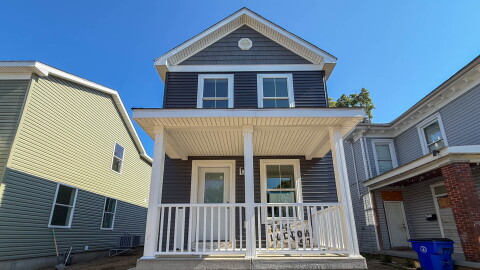 A two story home with a white porch and blue grey vinyl siding.