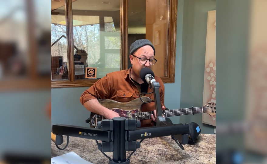 A man is singing into the microphone in a radio station studio, while playing the guitar.