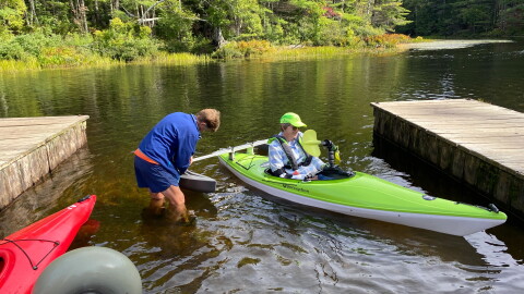 Cathy Webster assists a paddler in launching their adaptive kayak into Fish Creek.
