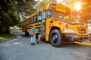 A young redheaded boy getting onto a school bus in sunshine.