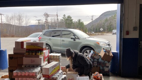 SNAP recipients line up at the New Hampshire Food Bank’s warehouse in Berlin, waiting for boxes of non-perishables and fresh produce. A New Hampshire Food Bank employee packs boxes for the people in line.