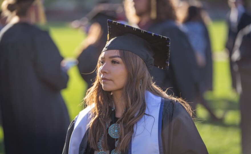 A person with long wavy hair is wearing a cap and gown.