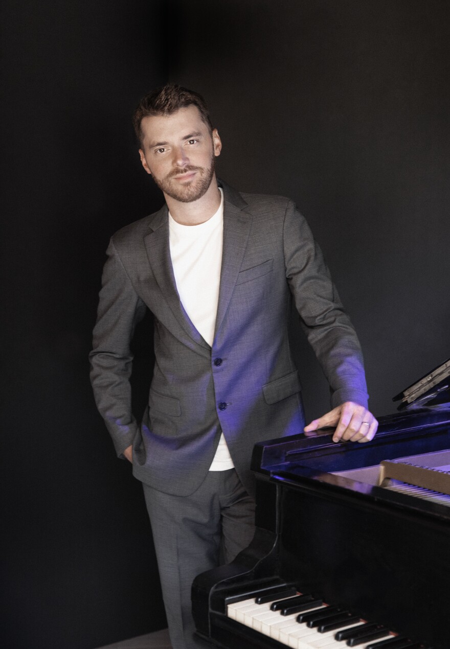 Dugan stands beside a black and white piano