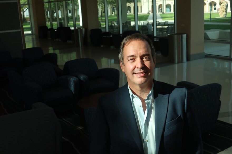 Carlos Diaz-Rosillo standing in the light. In the background is a large, dark and empty hall at Florida Imternational Umiversity.