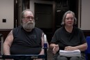 A man and a woman wearing black shirts, holding paperwork and a walker