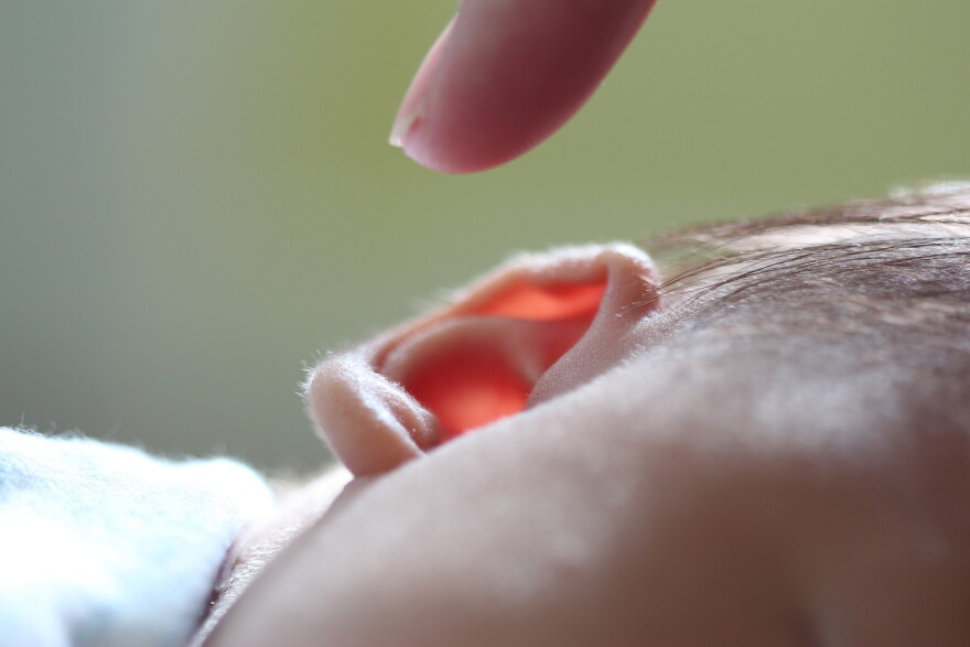 close up of the side of a child's face laying down, a finger points to the ear from above. jpg