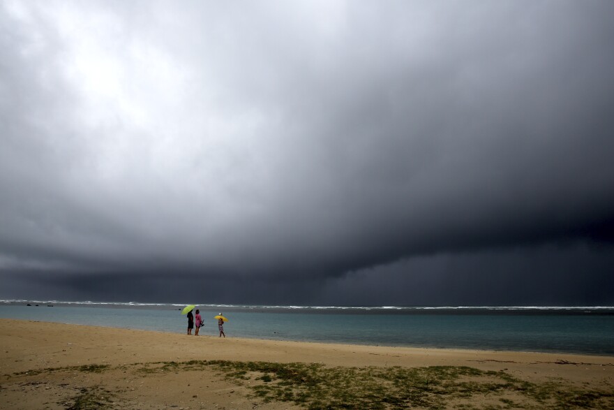 People watch storm clouds as it begins to rain in Honolulu on Monday. A strong storm packing high winds and extremely heavy rain flooded roads and downed power lines across Hawaii, with officials warning Monday of potentially worse conditions ahead.