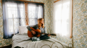 Flock of Dimes' Jenn Wasner playing the guitar on a bed