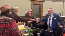A small group of men and women speak over a desk as one pair shakes hands.