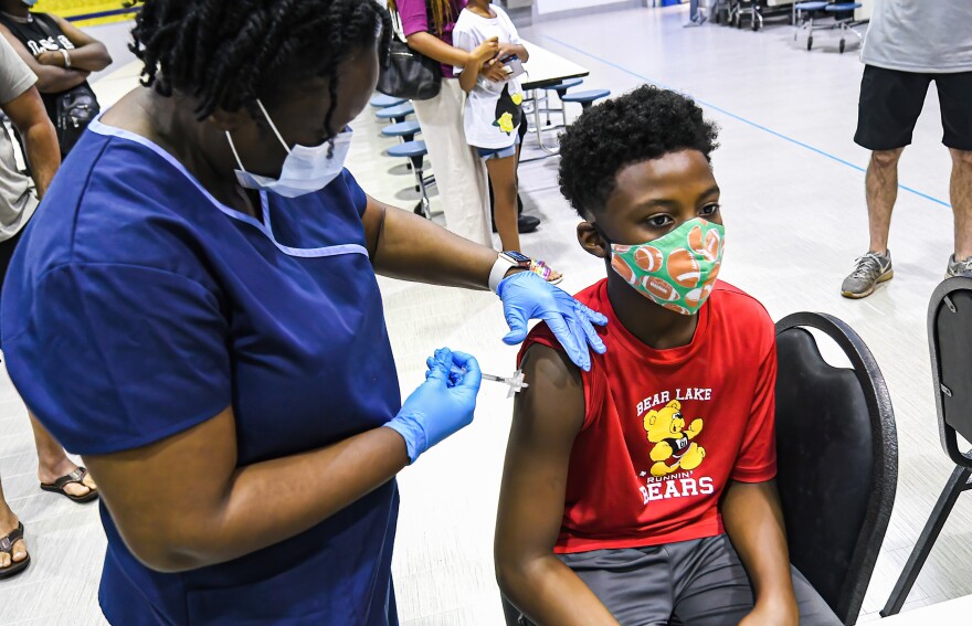 A boy gets a shot from a woman in a mask.