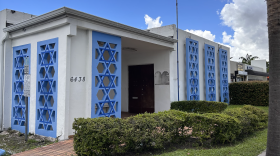 A white building decorated with blue stars of david at the entryways. A shadow is by the front door where a plaque once was.