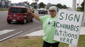 FILE - In this July 30, 2018, file photo, Zora Braun gestures to people as cars drive by a location in Oklahoma City where they can sign petitions for recreational marijuana and a constitutional amendment for medical marijuana. A group seeking to legalize recreational use of marijuana in Oklahoma refiled their petition on Friday, Dec. 27, 2019, after facing a fierce backlash over what the plan might do to the state's burgeoning medical marijuana industry. The latest petition was redrafted to make sure there were greater protections for the existing medical marijuana industry and its patients. (AP Photo/Sue Ogrocki, File)