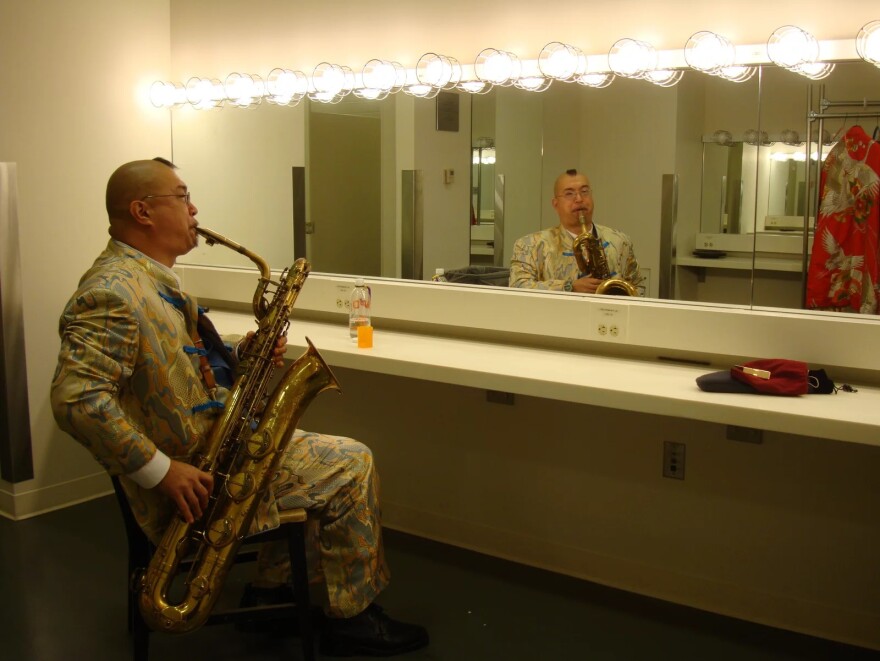 Fred Ho practices his baritone saxophone in a dressing room before a performance.