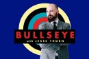 A man in a grey suit stands in front of a blue background with a red, blue, black, and cream target. A black text box reading "Bullseye with Jesse Thorn" is in the foreground.