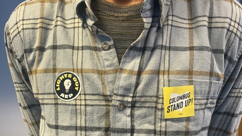 Columbus Stand Up cofounder Kwesi Low wears stickers recognizing the group and its campaign "Lights Out AEP" against American Electric Power's proposed rate increase at a public hearing in downtown Columbus on Dec. 9, 2025.