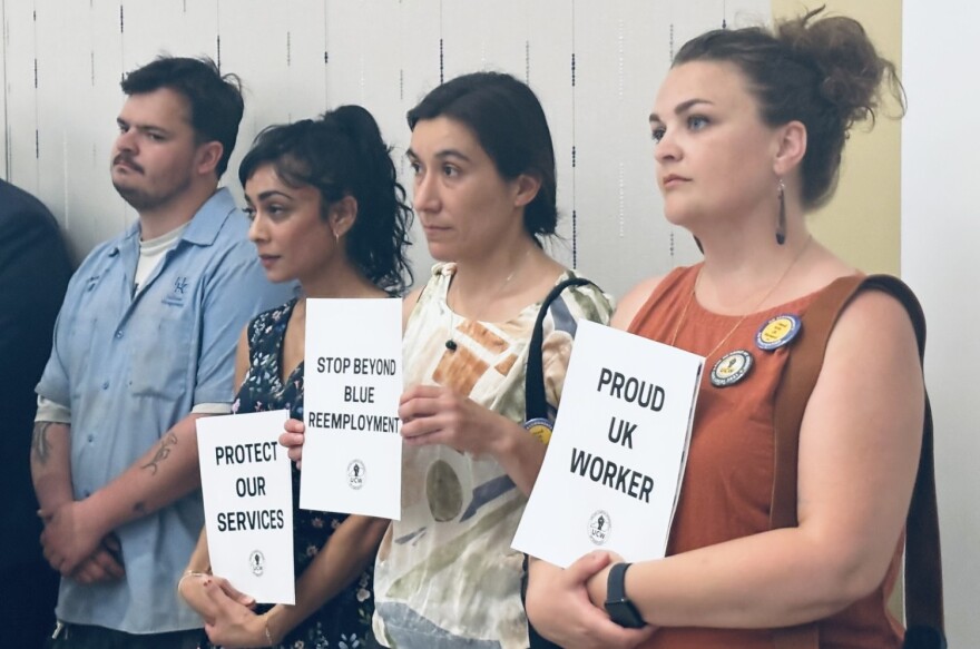 UK workers and advocates hold signs at a Board of Trustees meeting.