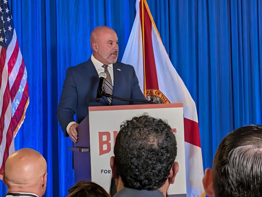 A man in suit speaks at a podium in front of a crowd